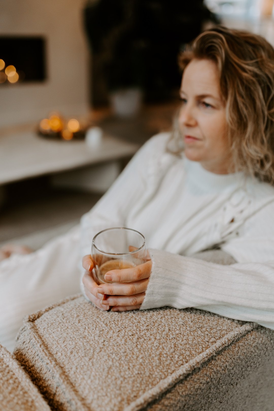 Vrouw in gedachten verzonken met een kop thee bij het haardvuur